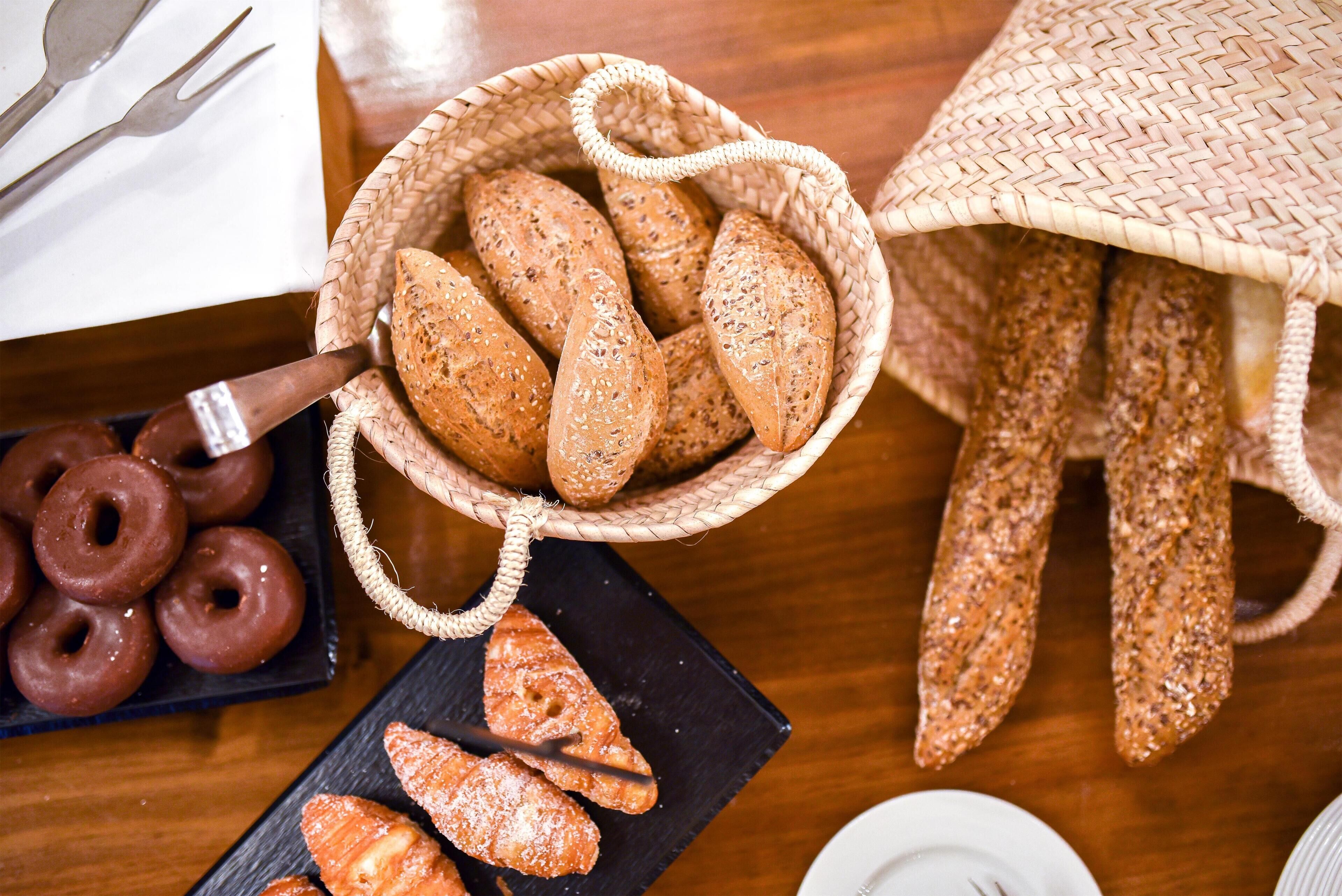 A basket of assorted breads and pastries on a wooden table.