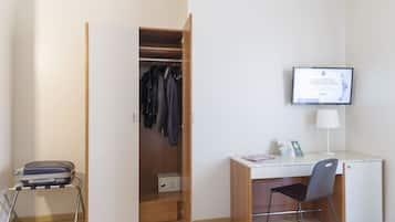 Habitación de hotel con armario de madera, un escritorio con silla, televisor y maleta sobre un carrito.