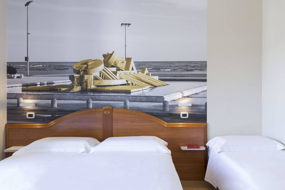 A hotel room with a bed, a nightstand, and a wall mural of a beach scene.
