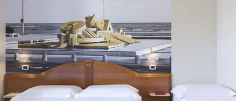 Habitación de hotel con cama, mesita de noche y un mural en la pared que representa una playa.
