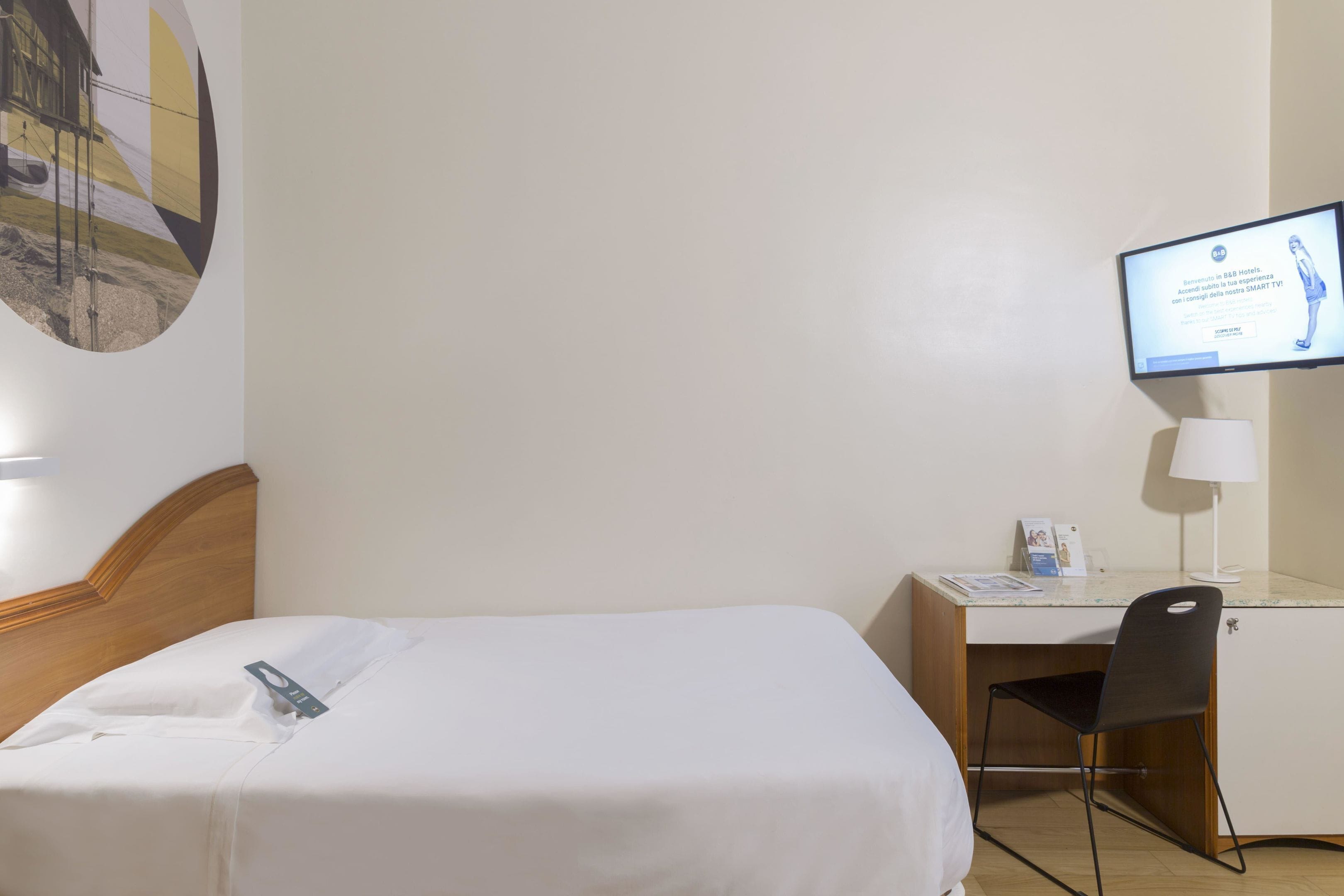 A hotel room with a bed, desk, chair, and a TV displaying a message.