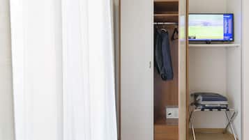 Habitación de hotel con armario, televisión y carrito para equipaje.