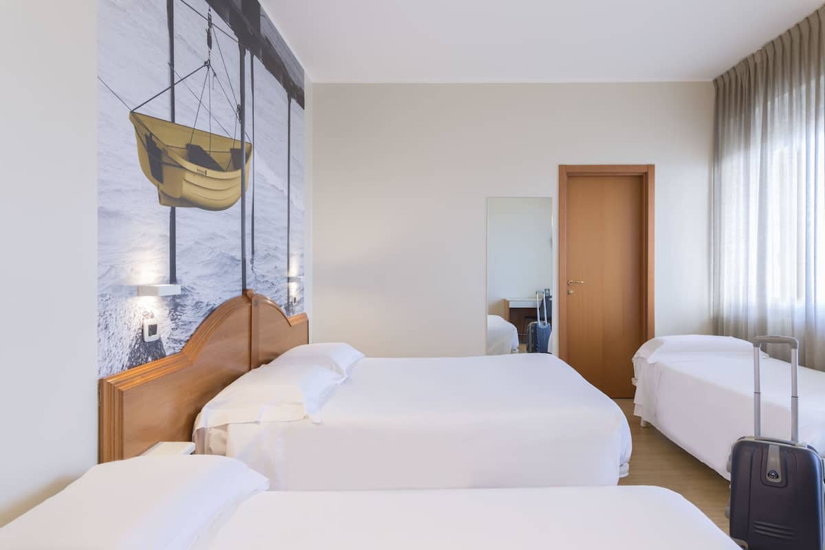 A hotel room with two beds, a wooden headboard, a hanging boat chair, a wooden door, and a suitcase.