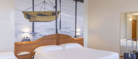 A hotel room with a large bed, a wooden headboard, a hanging boat decoration, and a suitcase.