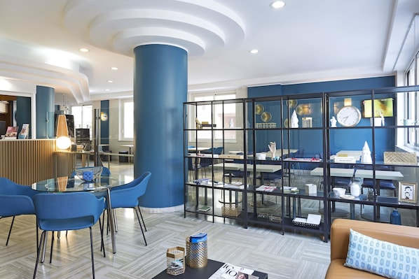 Un vestíbulo moderno con una mesa de vidrio, sillas azules, un sofá y un separador decorativo de vidrio con estantes.