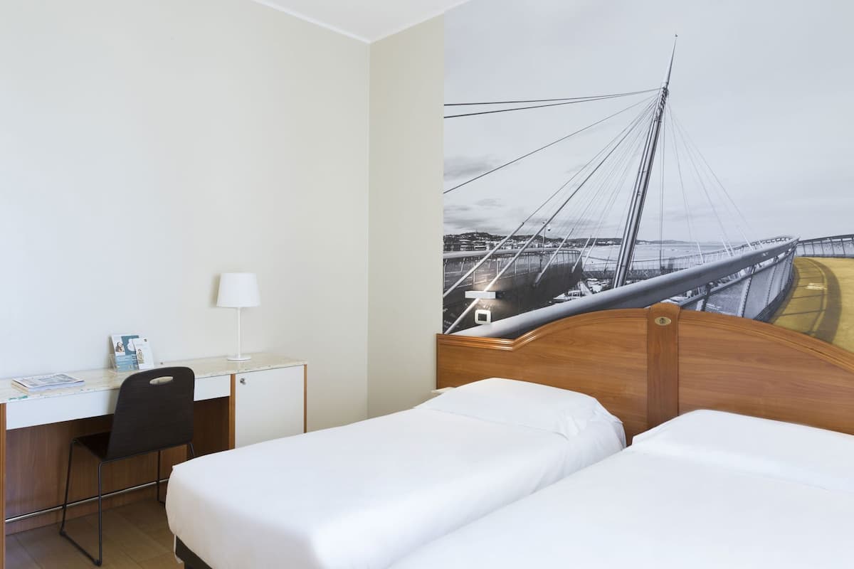 A hotel room with a bed, desk, chair, and a large wall mural of a bridge.