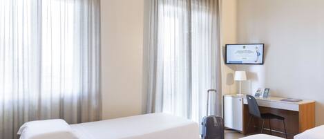 Habitación de hotel con dos camas, un escritorio, una silla, un televisor y una maleta.