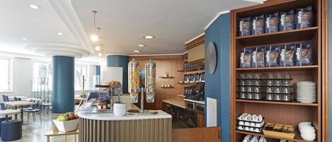 Un café moderno con mostrador, zona de estar y estanterías llenas de café en grano y utensilios de cocina.