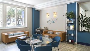 Ein modernes Wohnzimmer mit einem Glastisch, blauen Sesseln, einem beigen Sofa und einem Bücherregal.
