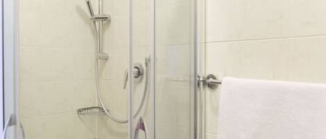 A glass-enclosed shower with a handheld showerhead and a wall-mounted faucet.