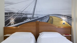 Ein Hotelzimmer mit einer großen Wandmalerei einer Brücke, einem hölzernen Kopfteil, zwei Betten mit weißen Bettwäsche und Nachttischen mit Lampen.