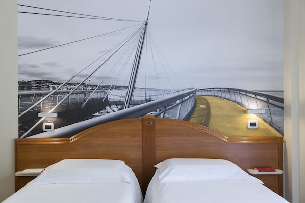 A hotel room with a large mural of a bridge, a wooden headboard, two beds with white linens, and bedside tables with lamps. - B&B Hotel Pescara (Pescara)