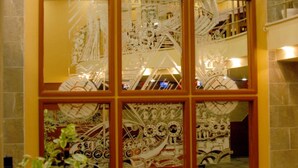A large window with intricate designs, a tiled floor, and a potted plant in the foreground. - Anzac Hotel (Çanakkale)