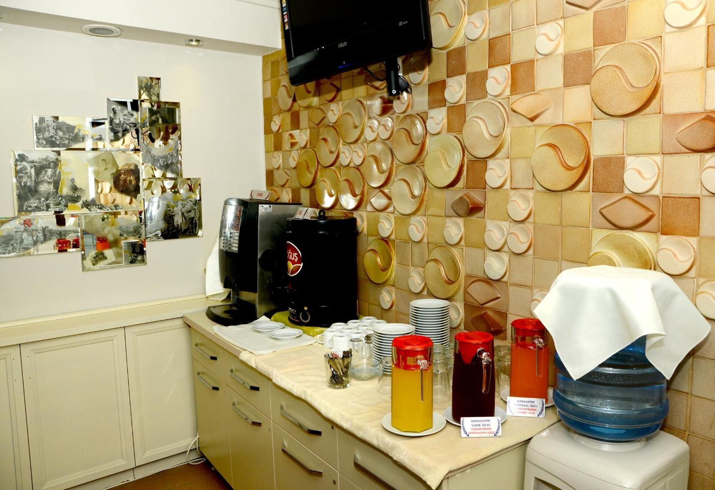A kitchen area with a buffet setup, including a refrigerator, coffee machine, and various food and drink containers.