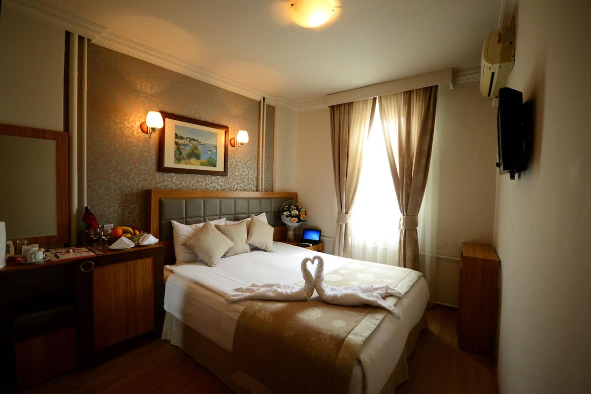 A hotel room with a large bed, a desk with a computer, and a wall-mounted TV.
