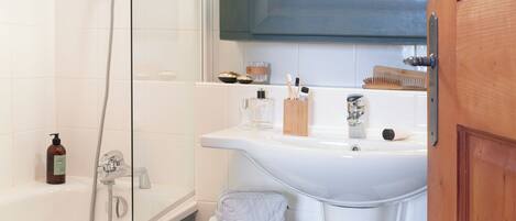 A bathroom with a bathtub, shower, and sink, with towels and toiletries on the counter.