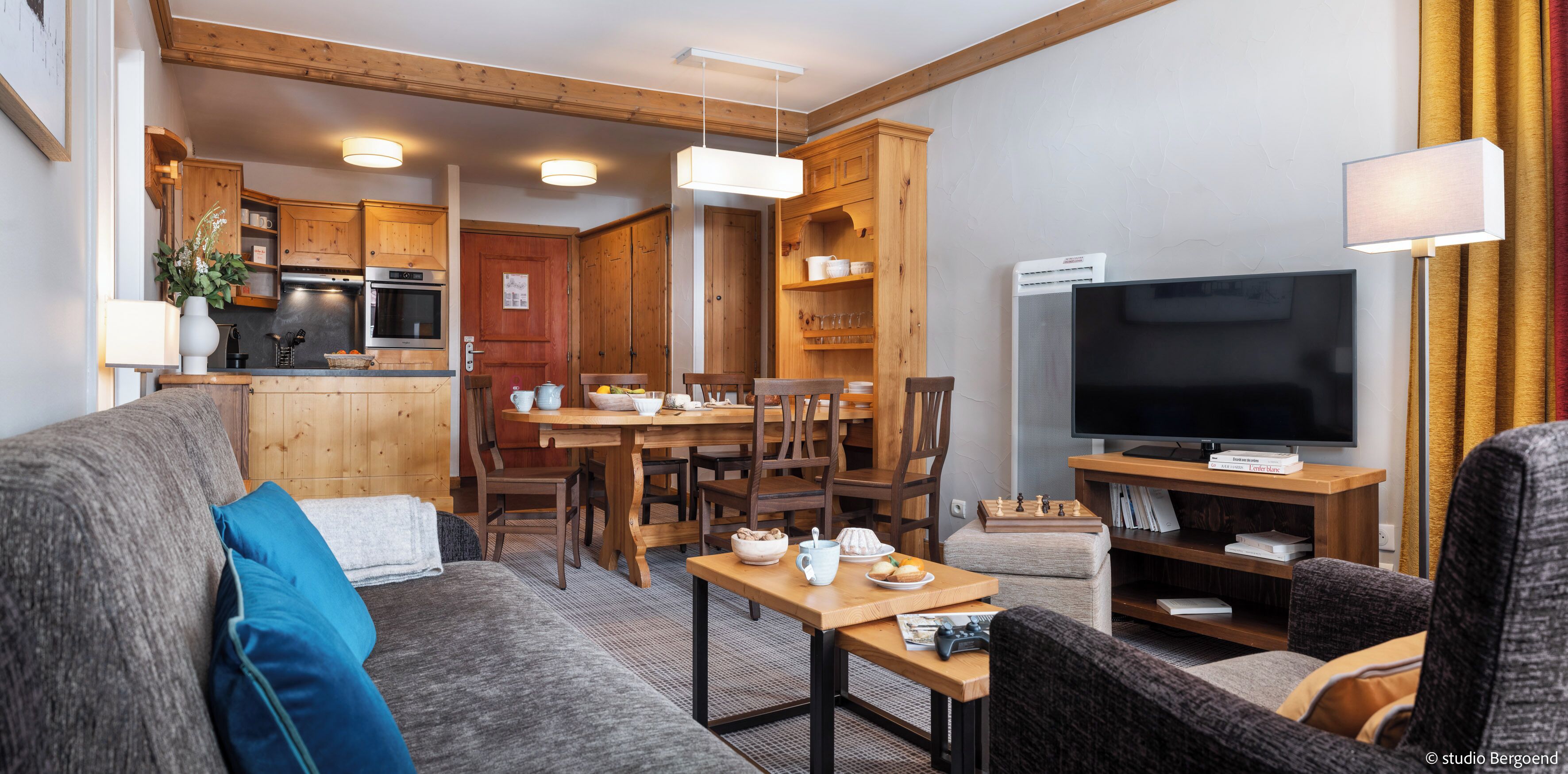A cozy living room with a grey sofa, a wooden dining table, and a flat-screen TV.