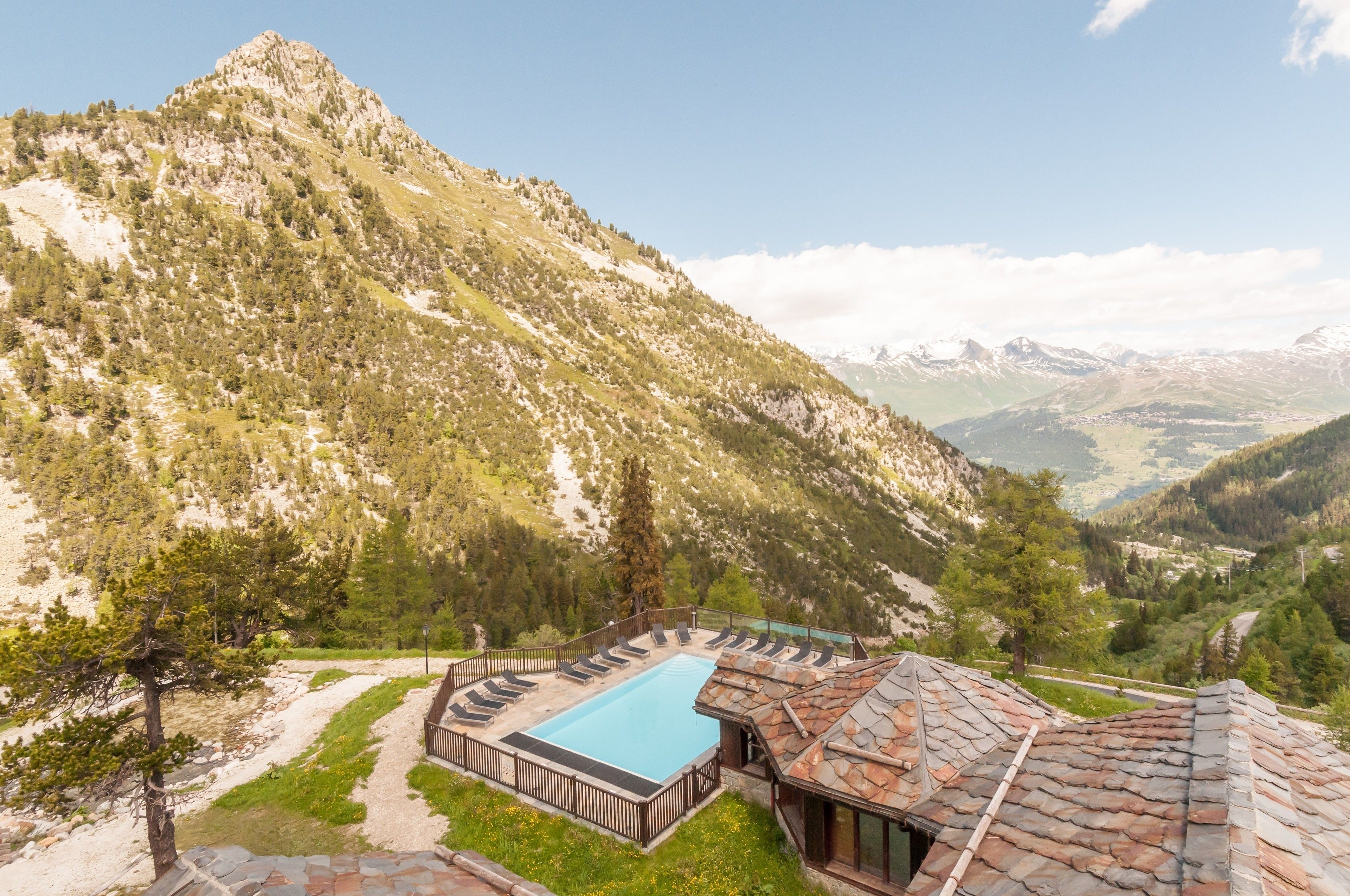 A mountain resort with a swimming pool, stone-roofed building, and a view of the surrounding mountains.
