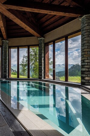 Une piscine offrant une vue dégagée sur les montagnes grâce à de grandes fenêtres.