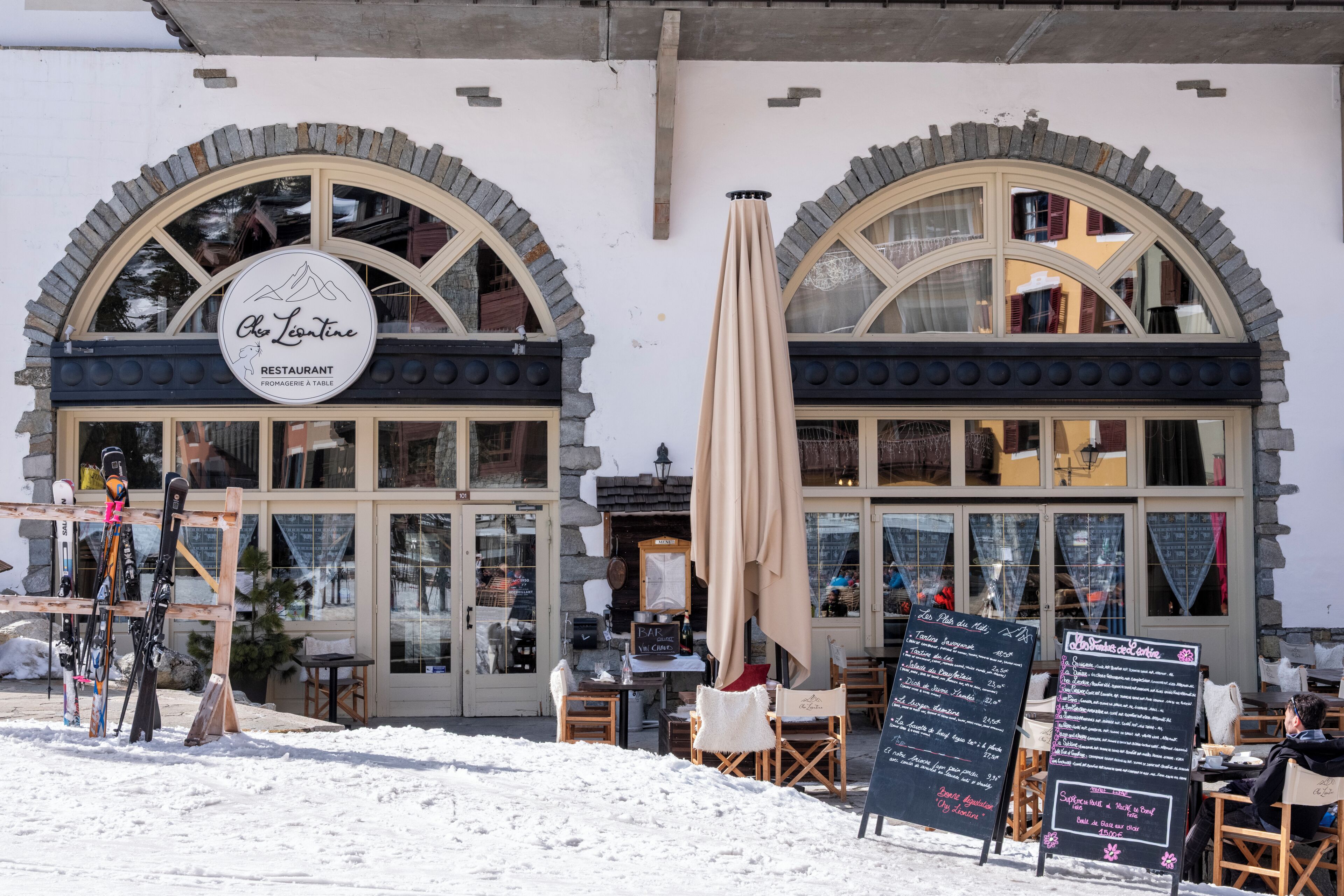 A restaurant with a sign reading 'Chez Laurentine,' outdoor seating with tables and chairs, and a menu board.