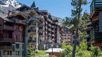 Ein traditionelles Holzgebäude mit mehreren Balkonen und einer Steinaußenwand, vor einer Bergkulisse gelegen.