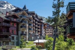 Un edificio de madera tradicional con varios balcones y fachada de piedra, con montañas al fondo.