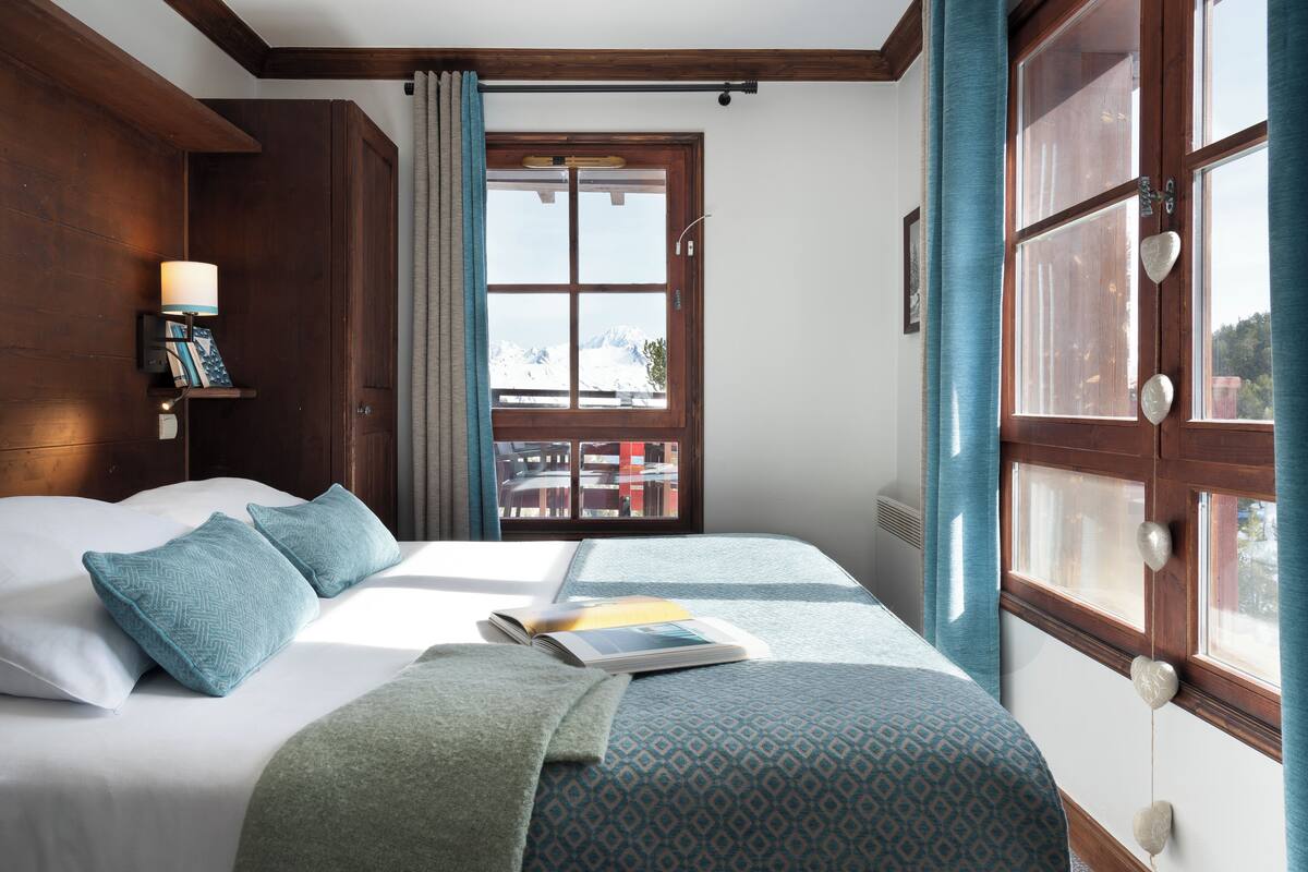 A neatly made bed with pillows, a bedside lamp, and a book on the bed.