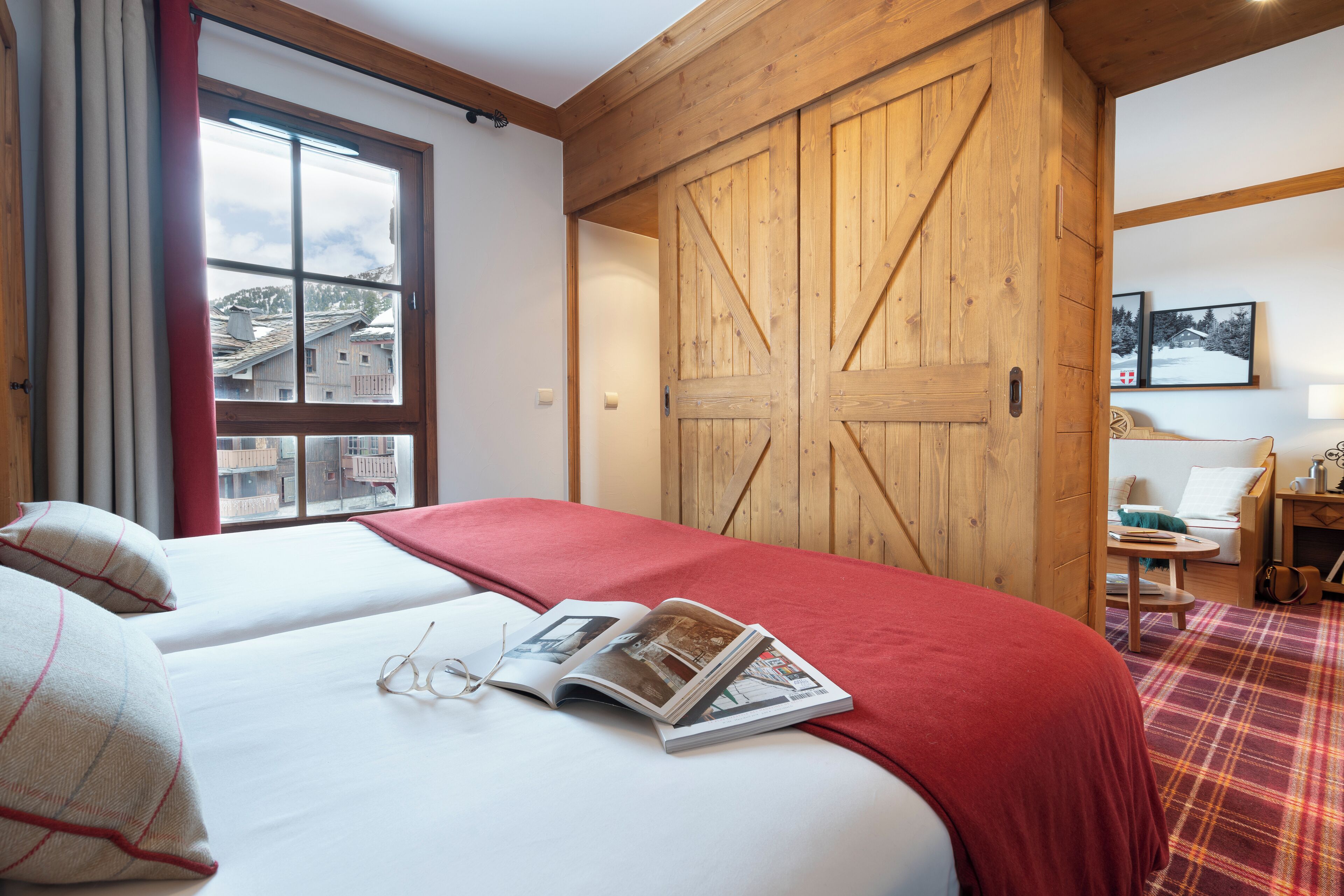 Un dormitorio con un ventanal grande, un armario de madera, una cama con una colcha roja y una alfombra escocesa.