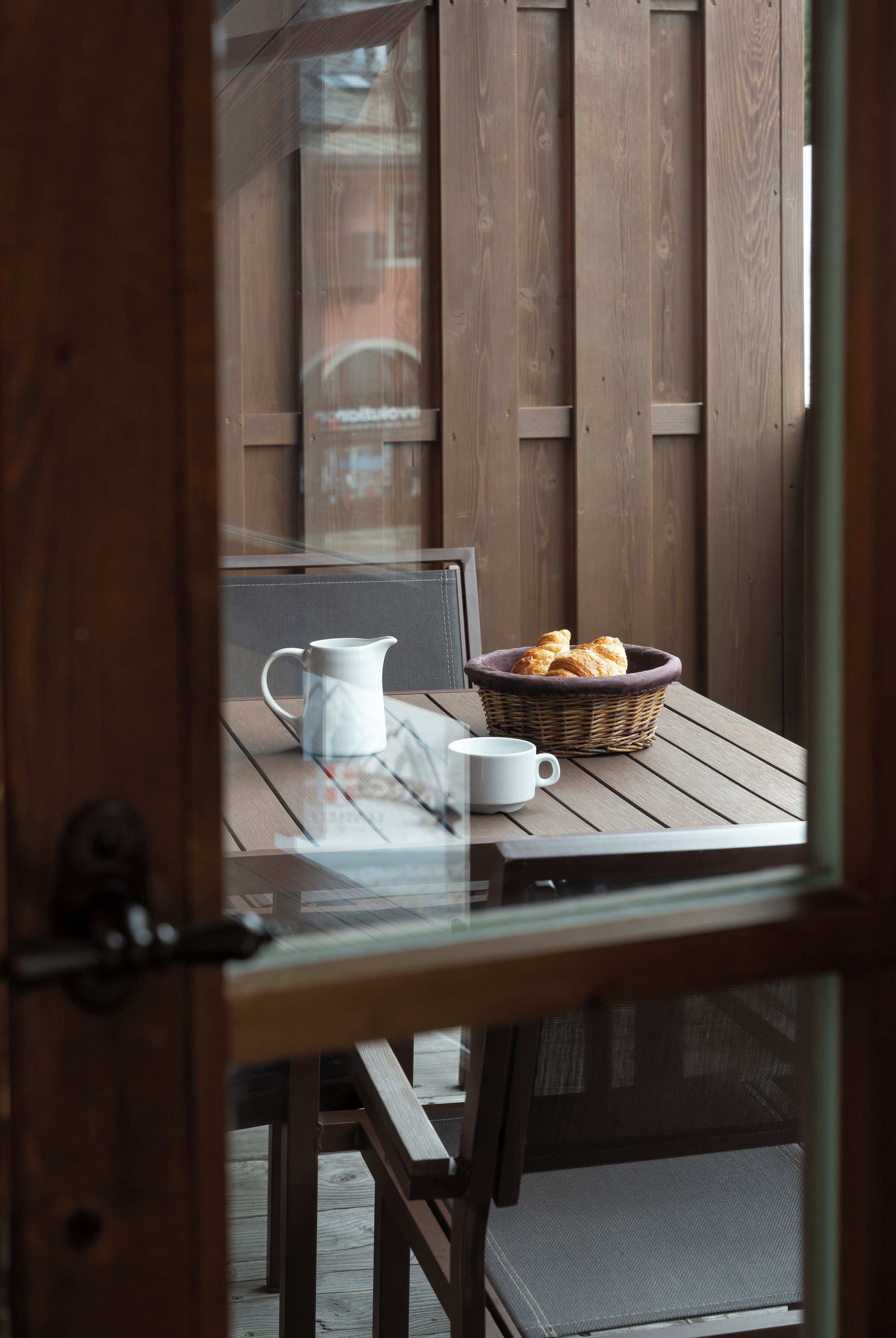 A wooden table with a white pitcher, a white cup, and a basket of bread.