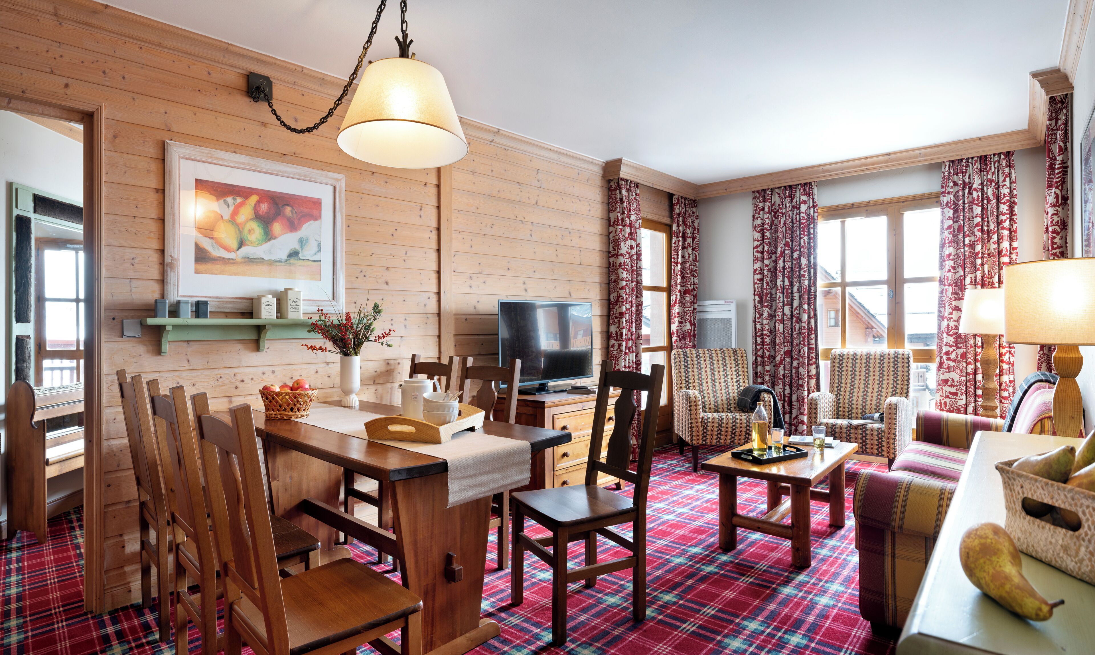 A cozy room with wooden walls, a dining table with chairs, a television, and a sofa.