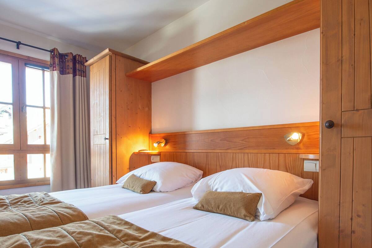 A double bed with a brown blanket, wooden headboard, and a nightstand with a lamp.