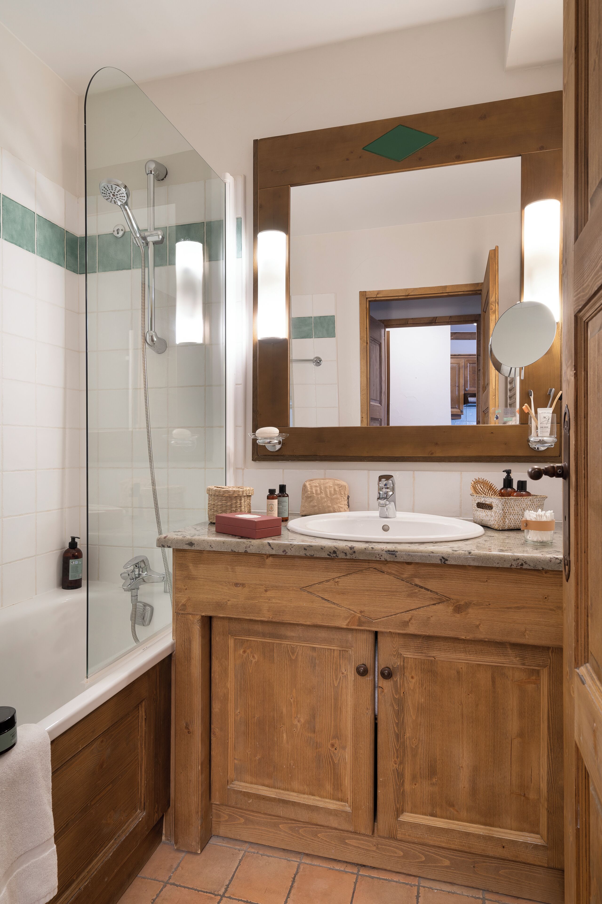 A bathroom with a glass-enclosed shower, wooden cabinets, a marble sink, and a large mirror.