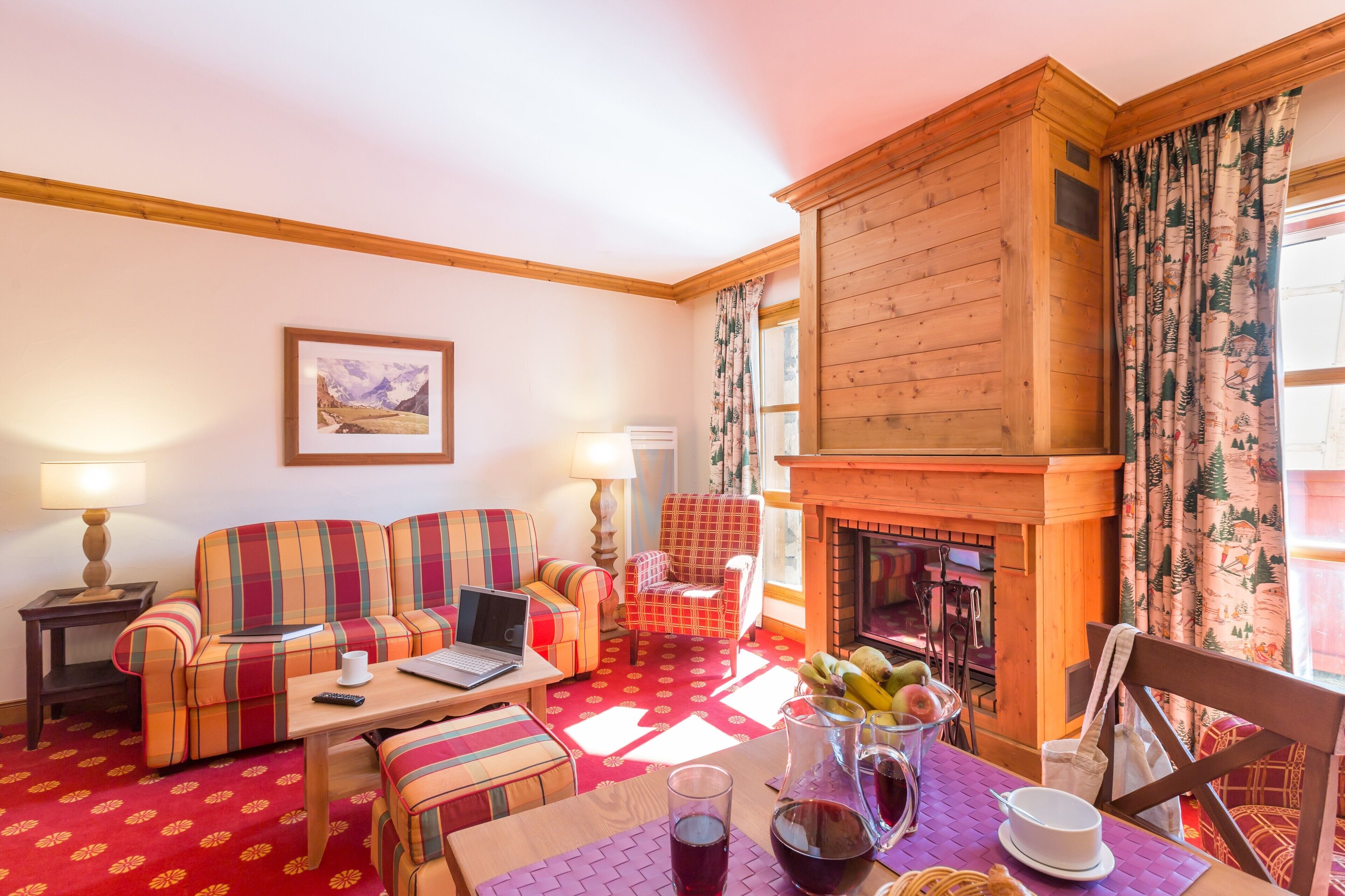A cozy room with a fireplace, a sofa, a chair, and a table with a laptop and a glass of wine.
