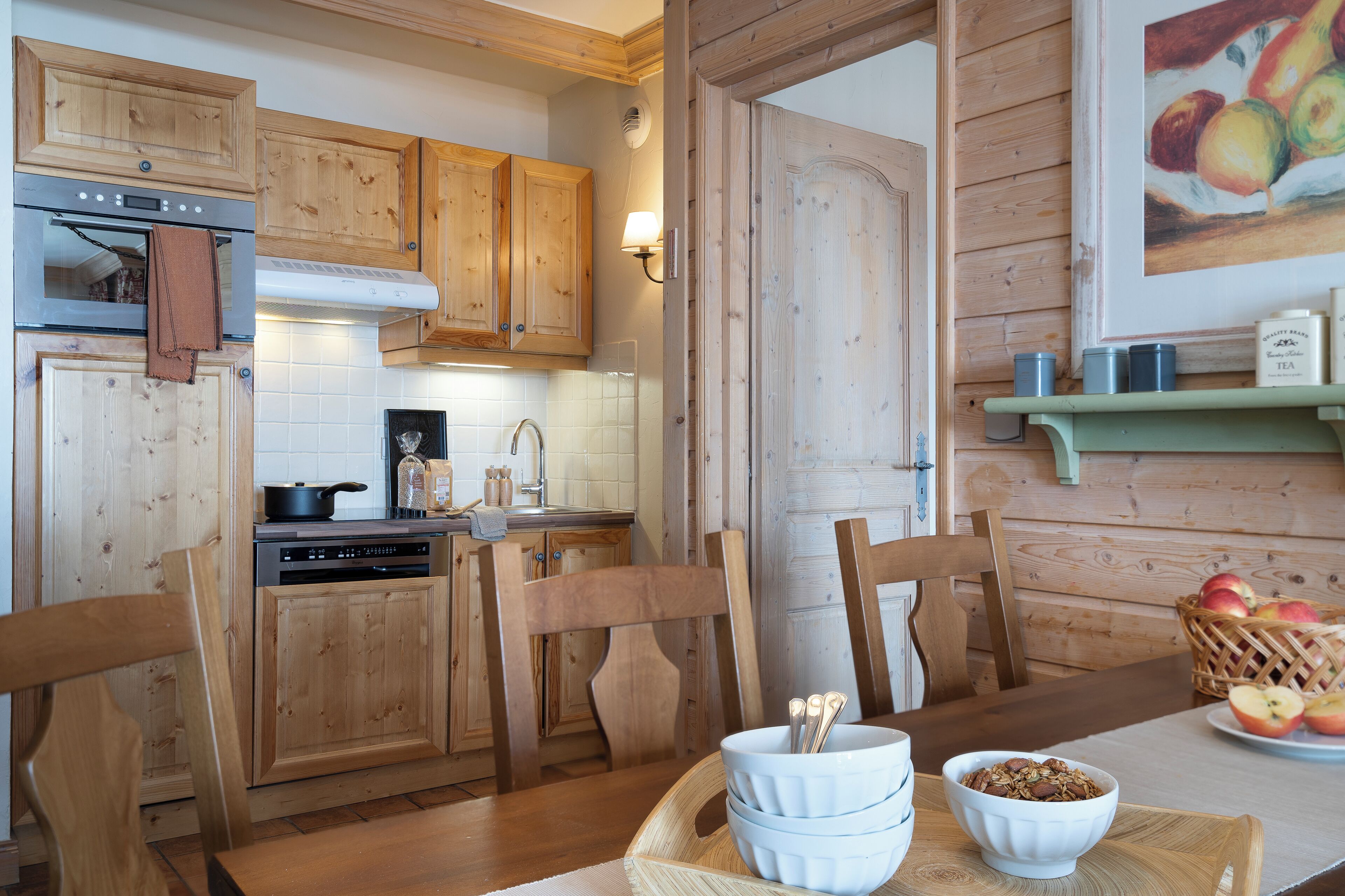 A wooden kitchen with cabinets, a stove, and a dining table with chairs. There is a bowl of cereal on the table.