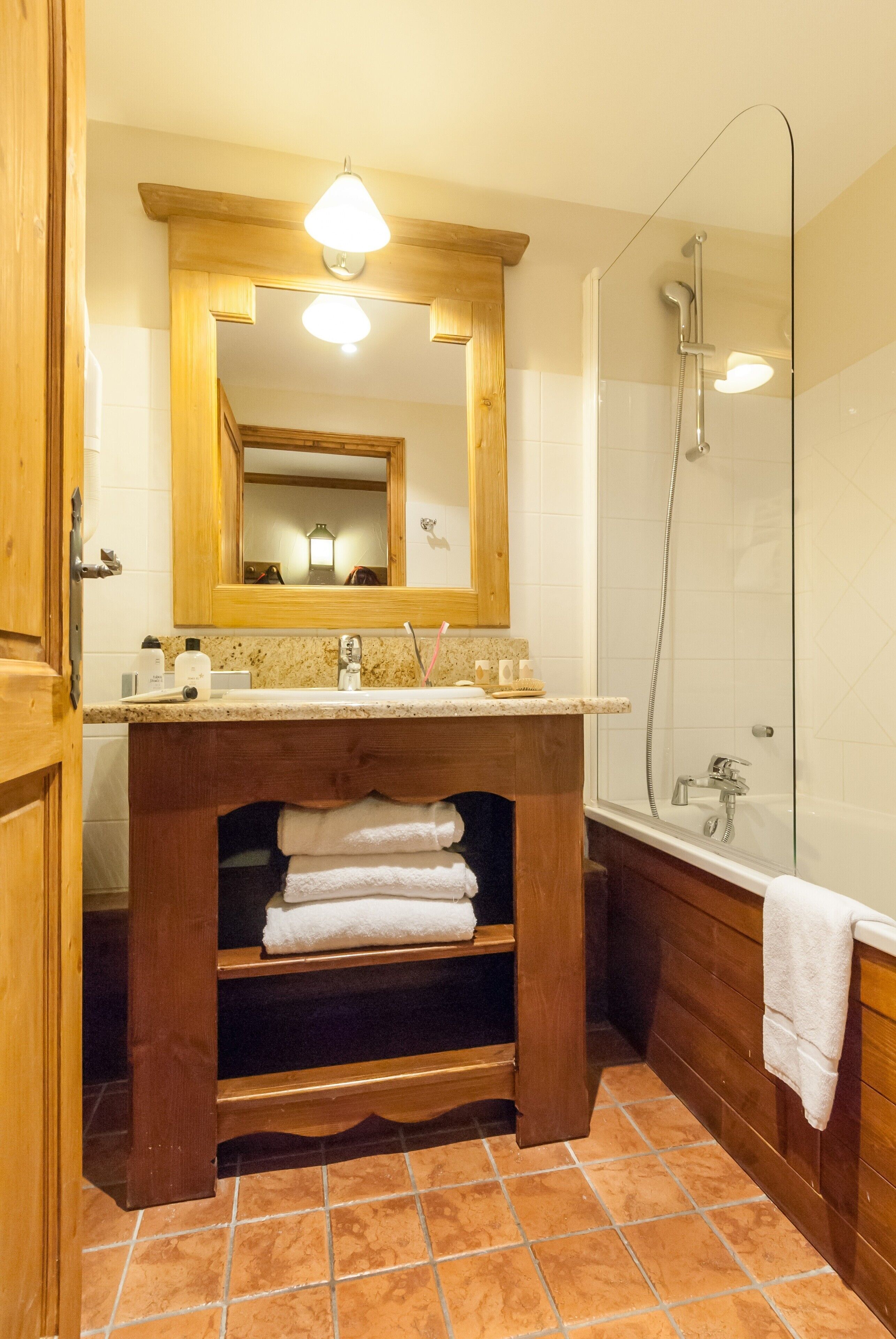 Un baño con tocador de madera, lavamanos, espejo, ducha y toallero.