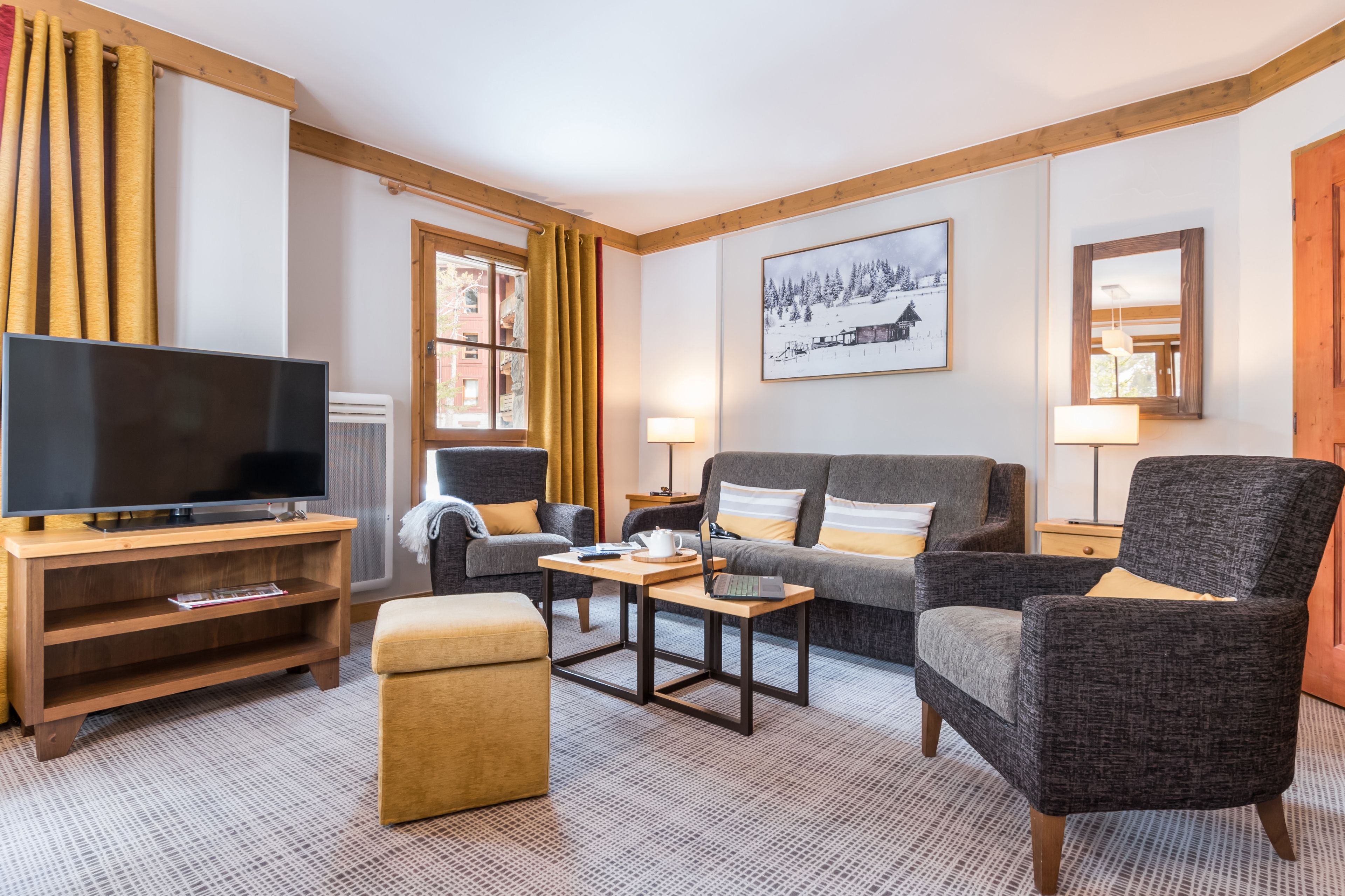 A modern living room with a flat-screen TV, a sofa, a chair, a coffee table, and a small ottoman.