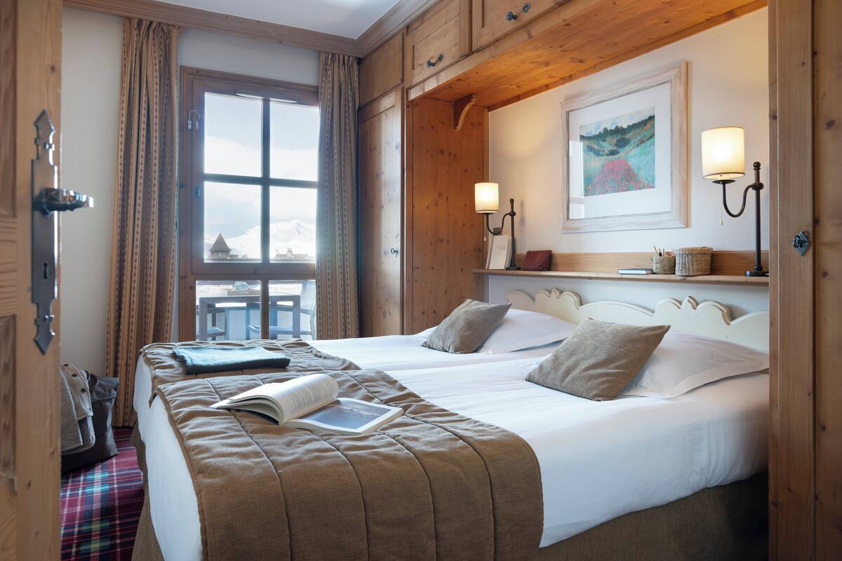 A hotel room with two beds, a wooden ceiling, a large window, and a painting on the wall.