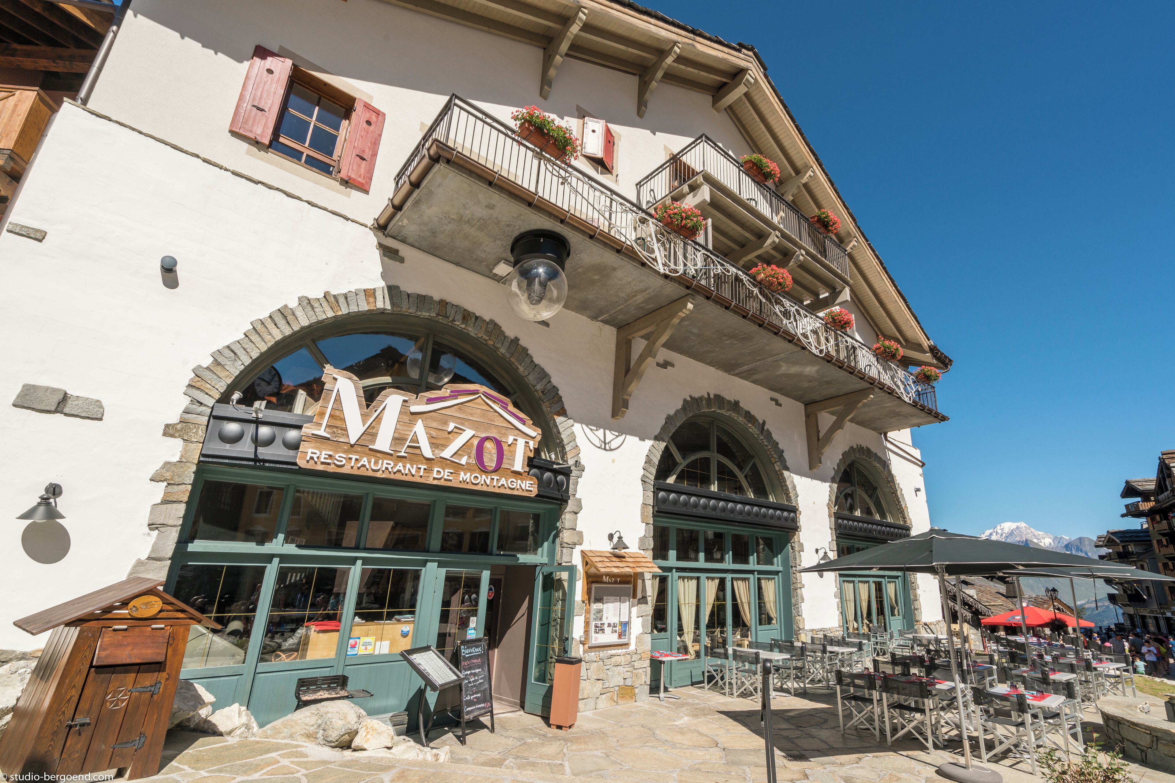 A restaurant with outdoor seating, stone facade, and mountain views.