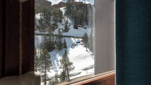 Vista desde una ventana a un complejo turístico de montaña con telesilla, paisaje cubierto de nieve y pinos.