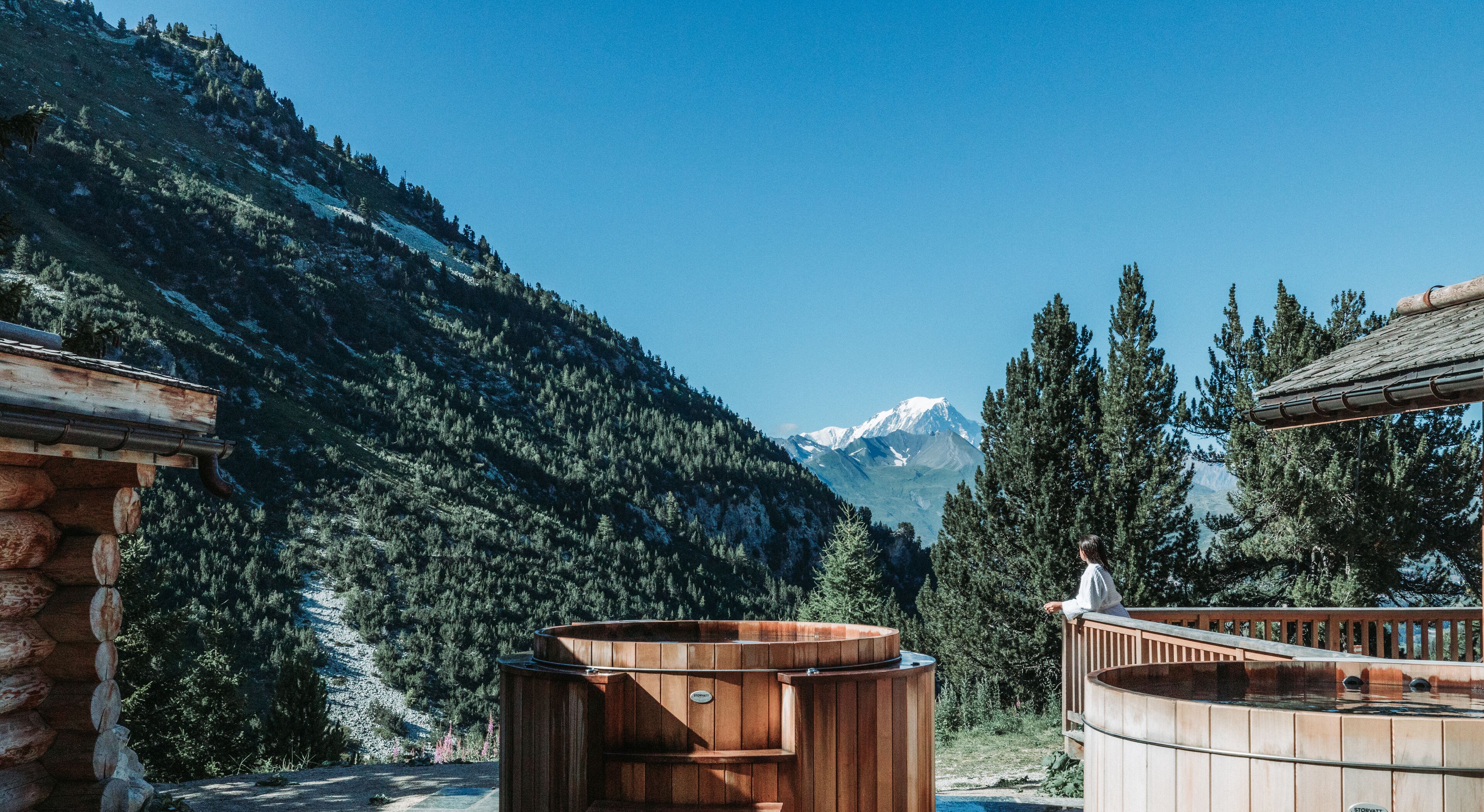 Tinaja de madera y paredes de piedra en zona montañosa, con vistas a picos nevados.