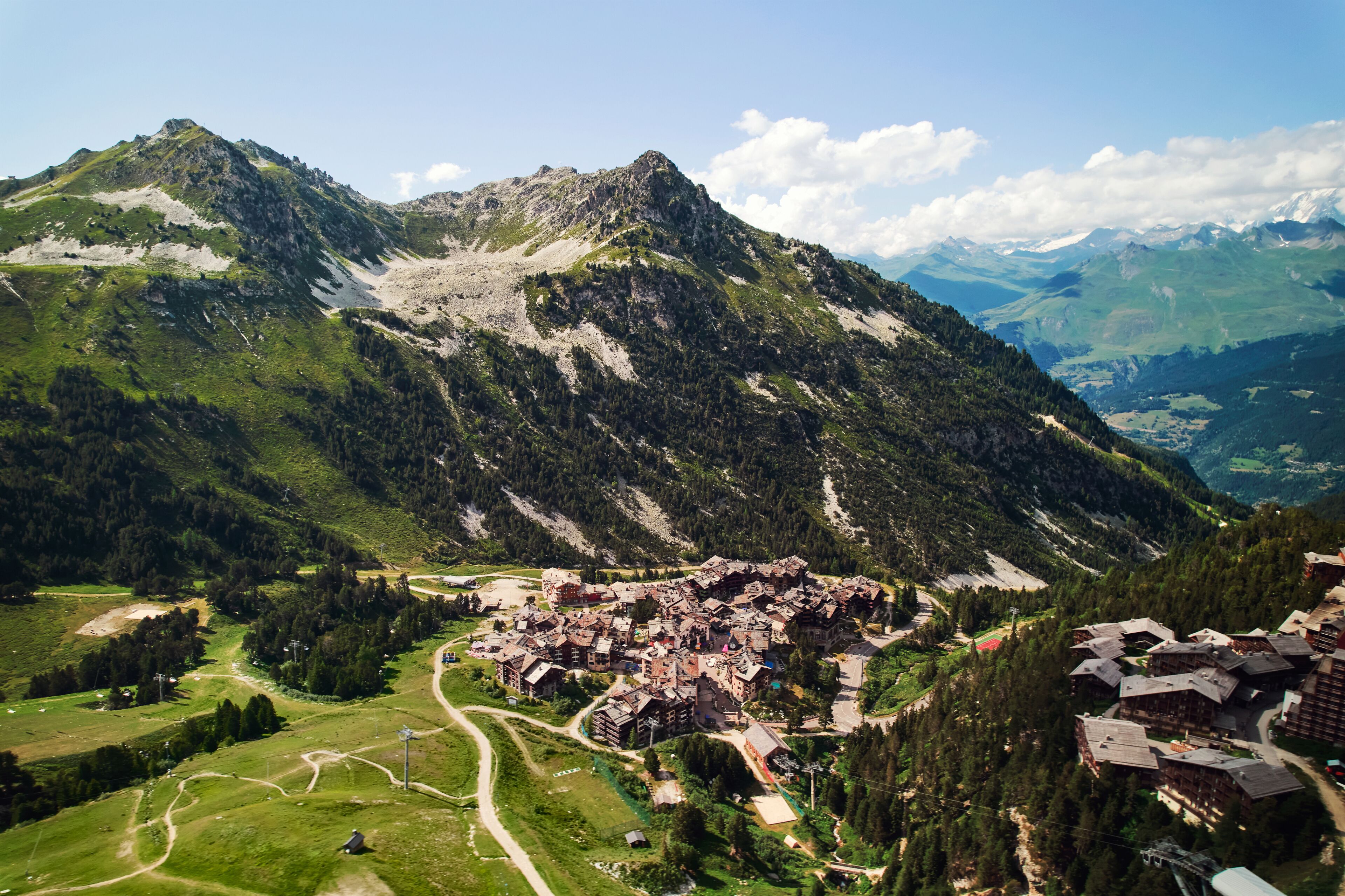A mountainous village with traditional wooden buildings, a winding road, and a clear sky.