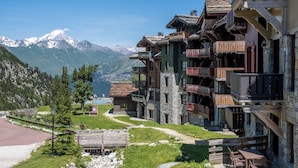 Un albergue de montaña con varios balcones, arquitectura de piedra y madera, y vistas a montañas nevadas.