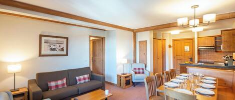 A cozy living room with a sofa, armchairs, a coffee table, and a dining area with chairs and a table set for a meal.