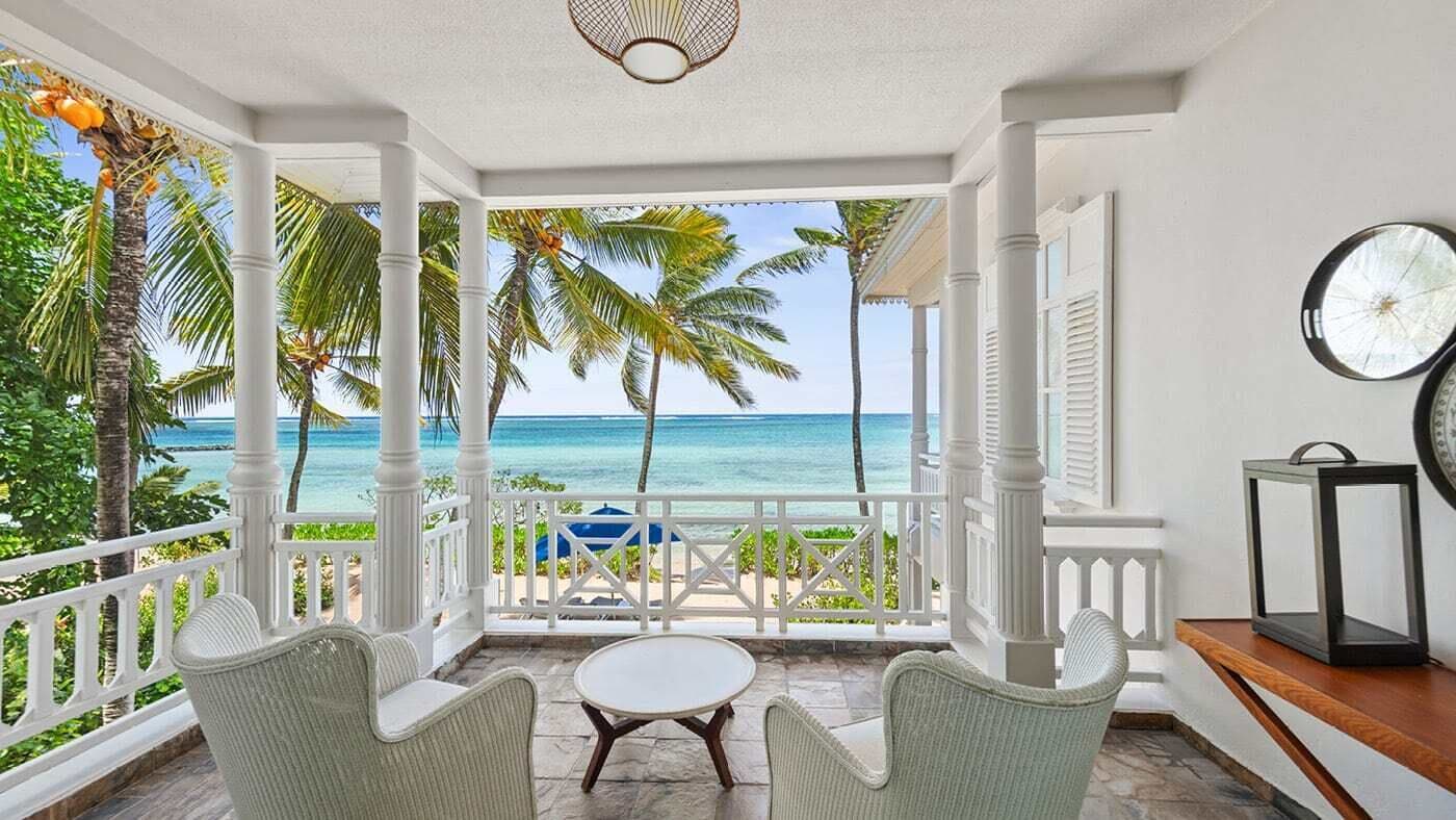 Un balcon avec vue sur l’océan, des colonnes blanches et des meubles en osier.