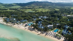 An aerial view of a coastal resort with beachfront villas, a swimming pool, and lush greenery.
