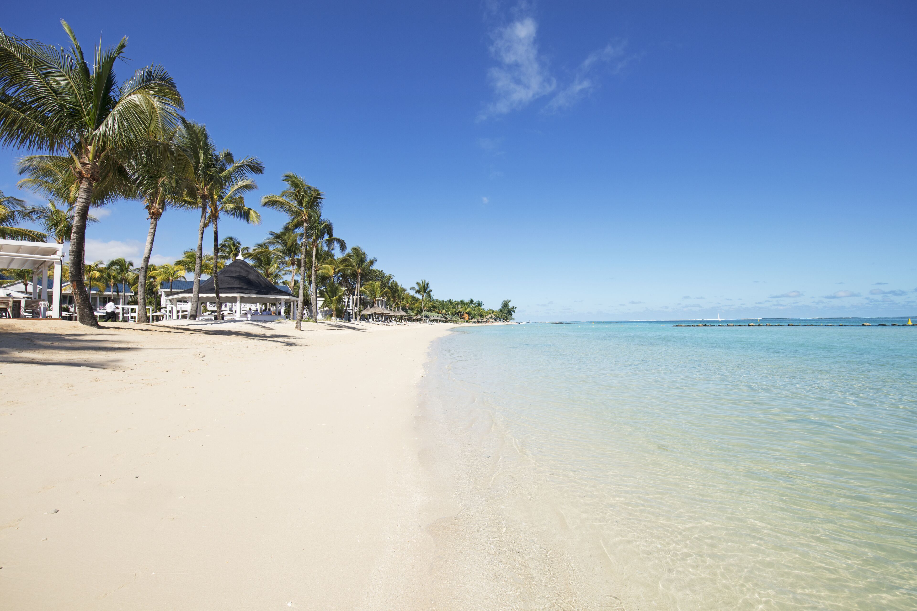 A beach with clear water, palm trees, and a white building with a black roof.
