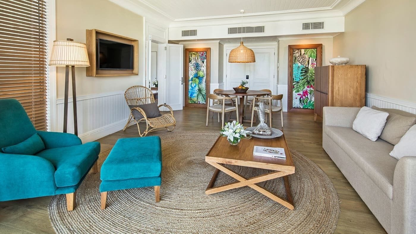 A spacious living area with a sofa, teal armchairs, a coffee table, a television, and a dining area with a table and chairs.