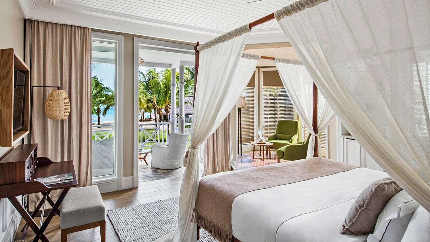 A bedroom with a canopy bed, a desk, and a view of the outdoor area.