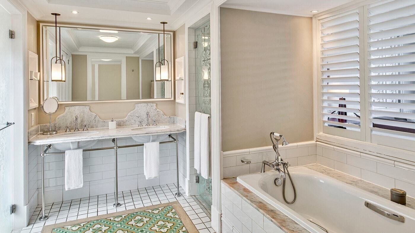A bathroom with a large mirror, two sinks, a bathtub, and a patterned rug.