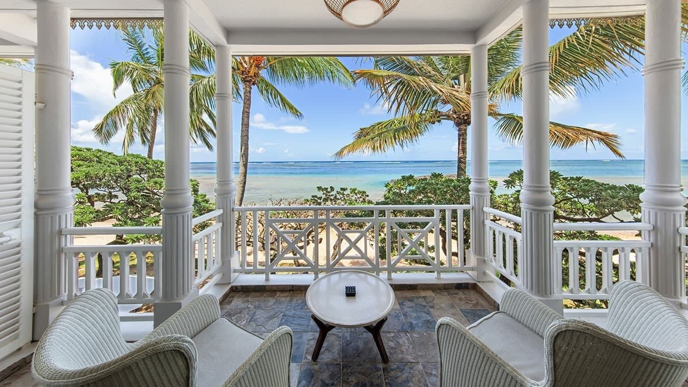 A covered outdoor area with white columns, a small round table, and two wicker chairs.